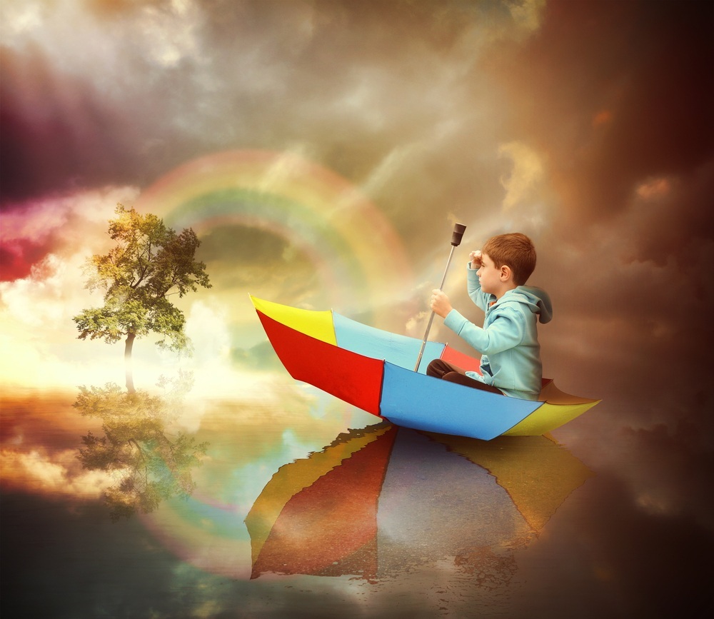 Criança sentada em um guarda-chuva como um barco, olhando para uma árvore com arco-iris atrás - foto: Angela Waye/ShutterStock.com