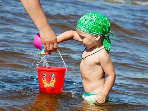 Criança dentro do mar enchendo baldinho com água - ShutterStock